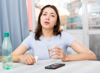 Upset girl suffering from troubles at table with bottled water