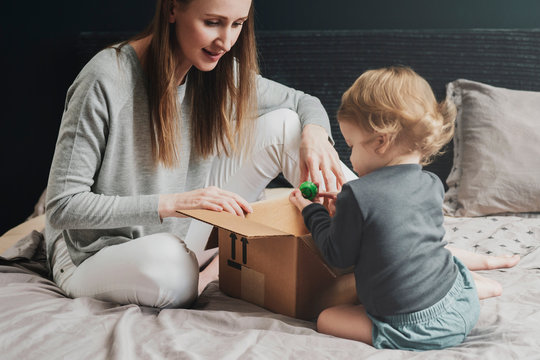 Woman and little child playing with big cardboard box. Mother putting things into package. Female purchasing products for famliy online and receiving them quickly at home address. Easy online payment