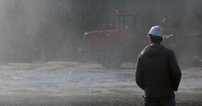 Marine coal terminal. A port worker in a white helmet stands with his back and watches the coal terminal work.
