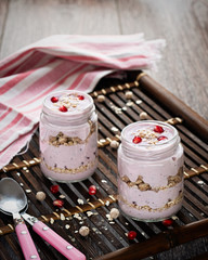 Yogurt with oatmeal, pomegranate seeds with teaspoons on a wooden background