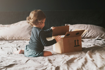 Little child playing with cardboard box on bed. Orders delivered by mail from international retail...