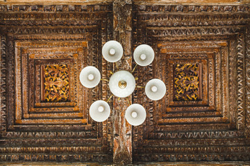 White chandelier on background of handmade wooden ceiling roof in balinese style with flowers and...
