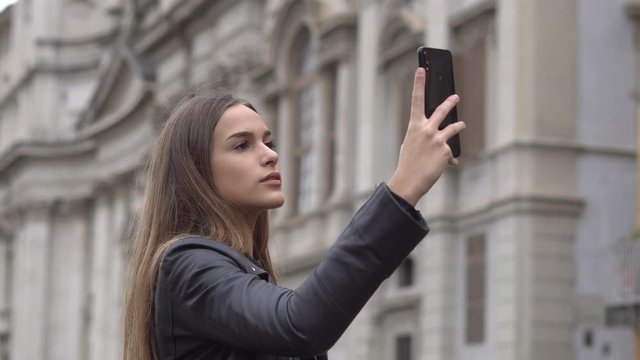 Stylish young woman holding and using a smartphone outdoors in Rome, Italy.