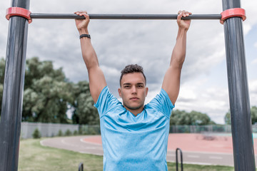 Fototapeta na wymiar male athlete pulls himself up on horizontal bar, crossbar on sports ground, in summer city. Fitness motivation youth lifestyle. Free space for copy text. Sportswear T-shirt.