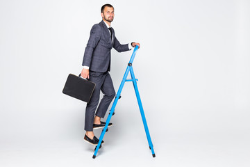 Full length portrait of a businessman with briefcase climbing a ladder isolated on white background