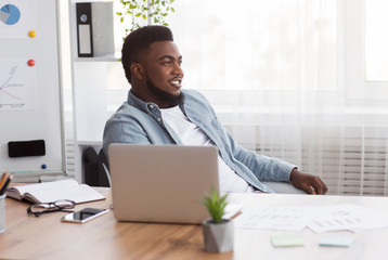 Naklejka premium Successful black businessman sitting at workplace with glad face expression