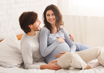 Happy pregnant couple relaxing on bed at home together