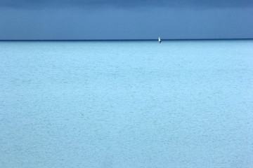 Obraz premium Small white yacht, turquoise blue sea and dark blue sky with clouds, a rainy day