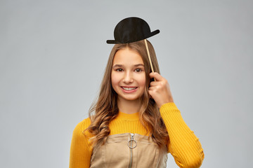 party props, photo booth and people concept - smiling teenage girl with black vintage bowler hat...