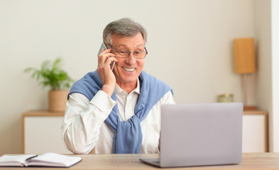 Senior Businessman Talking On Cellphone Working On Laptop In Office