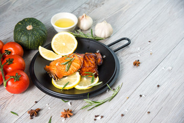 Grilled salmon steak on vintage wooden board with fork, olive oil, vegetables, herbs and spices on dark concrete background. Raw salmon fillet with vegetables, spices and lemon on wooden table.