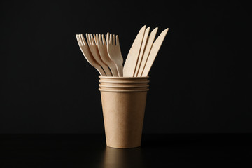 Eco - friendly cups with forks and knives on black background, space for text