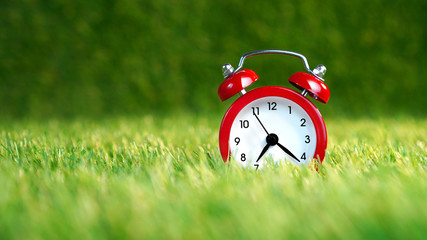 Red alarm clock on the green soft artificial grass lawn. Wake up background.