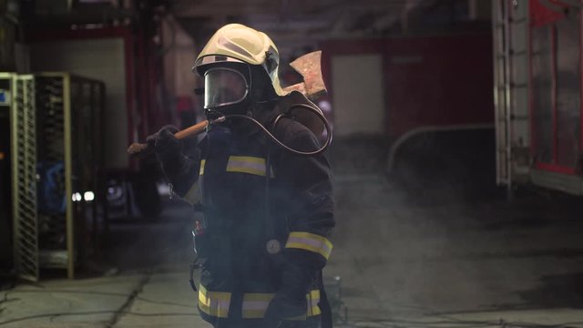 female firefighter portrait wearing full equipment, oxygen mask, and an axe, smoke and fire trucks in the background. 