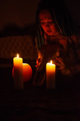 girl with blue dreadlocks conjures at night in a dark room, candle fire and a cow skull
