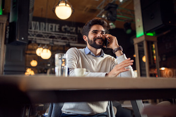 Handsome beard man talking on phone while sitting in cafe bar