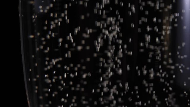 Sweet champagne. Glass with champagne stand on a wooden table against black background. Water drops, bubbles and foam on glass. Flutes with sparkling wine. New Year. Celebration. Close up. 4K