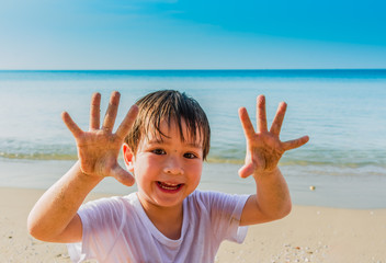 Portrait of happy little boy on summer beach with show sand on hands