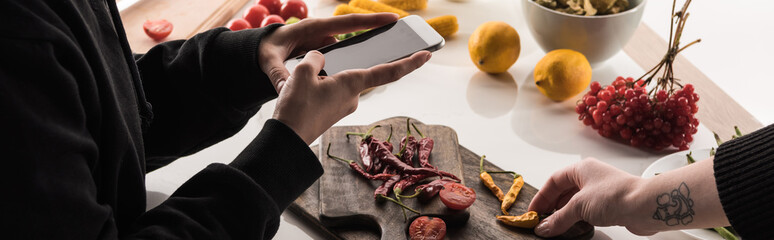 cropped view of two professional photographers making food composition for commercial photography on smartphone on wooden table