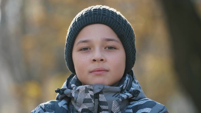 Handsome brunet boy in a hat standing and smiling outside in sunny park in autumn