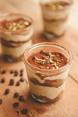 Tiramisu with pistachios and coffee in jars on a wooden countertop