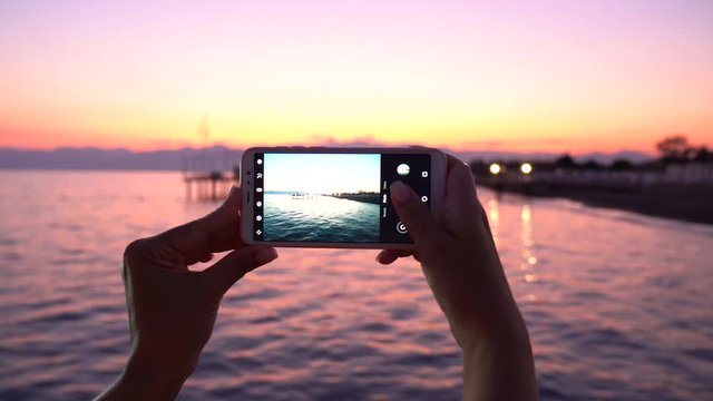 Closeup view of female hands holding modern mobile telephone taking beautiful travel pictures of amazing scenic sea landscape during sunset time. Real time 4k video footage.