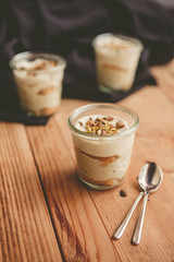 Tiramisu with pistachios and coffee in jars on a wooden countertop