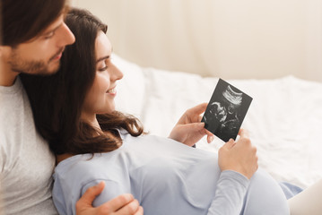 Happy pregnant woman and her husband looking at sonogram picture