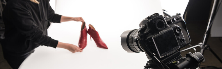 cropped view of commercial photographer making commercial photo shoot of female red heel shoes on white, panoramic shot