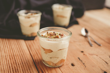 Tiramisu with pistachios and coffee in jars on a wooden countertop