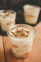 Tiramisu with pistachios and coffee in jars on a wooden countertop