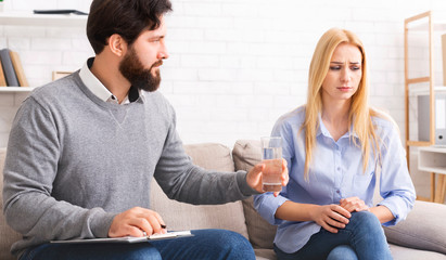 Psychologist offering glass of water to crying depressed woman