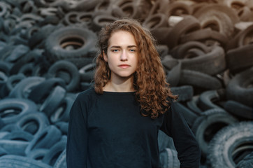 Obraz na płótnie Canvas Beautiful girl, curly hair, portrait on the background of a dump of old car tires. Looking at camera.