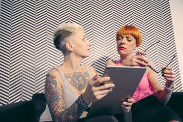 Due giovani amiche tatuate guardano un video sul tablet 