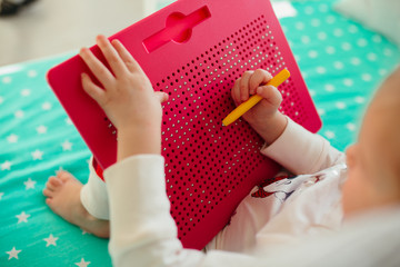 a child draws on a children's magnetic board with a yellow magnetic pen on a green crib