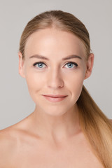 Fototapeta premium Studio portrait of attractive blonde caucasian woman with blue eyes and bare shoulders over white background. She is looking at camera with eyes wide open. Pure, smooth and flawless skin concept.