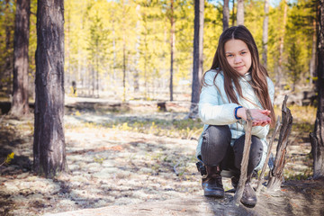 Fototapeta premium The beautiful girl in light jacket sits and has rest on an old snag in the spring forest.