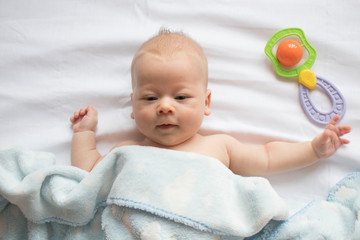 baby lying on his back on a white sheet with a rattle, top view