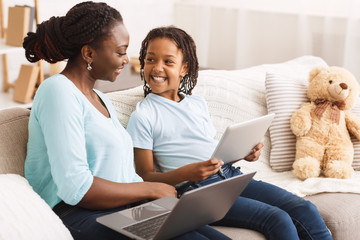 Black mom and daughter browsing Internet on sofa