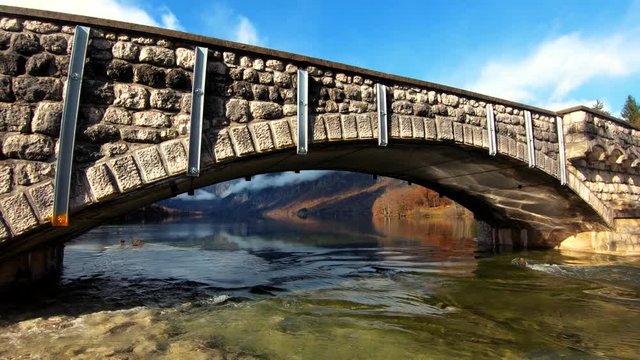 Slow motion right pan stone ancient arch bridge rapid river leaving Bohinj lake