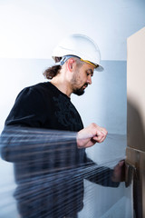 Male worker wrapping cardboard boxes in a stretch foil. A man packing cartons in a warehouse in a...
