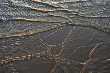 Pequeñas olas en una playa al atardecer formando líneas abstractas