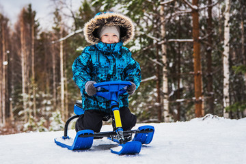 Fototapeta na wymiar Little boy on snow-scooter