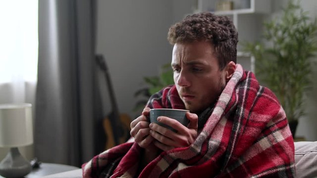 Cold man drinks tea on the sofa in the living room