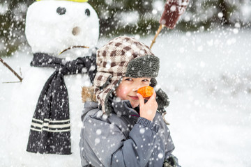 Winter fun, happy funny boy with carrot enjoy winter holiday over winter scenery with upset snowman...