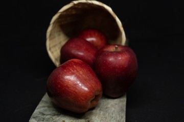 Red Apples in wooden basket on black background.