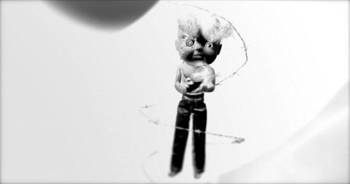 CREEPY-LOOKING DOLL, WITH A GIANT HEAD, IS SUSPENDED WITHIN BARBED WIRE.  NEGATIVE SHOT IN C4K, 10 BIT.