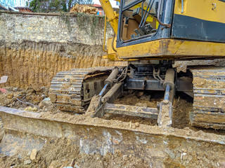 Excavator yellow bulldozer on site working on excavation business with earth and mud around, digging the ground for new building construction