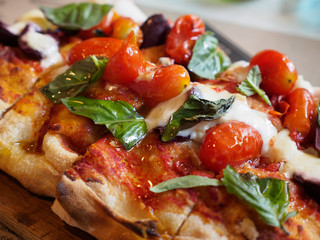 Closeup macro detail of a Margherita pizza topped with basil, cherry tomatoes, and Burrata cheese, served at an authentic Italian restaurant. Bangkok, Thailand. Travel and cuisine.