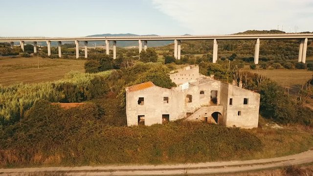 Aerial: Pan over ruins of a farmers house in, big bridge with cars in the background